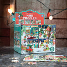 A boxed set of festive mini puzzles displayed on a tabletop, with several loose puzzle pieces in front. The packaging shows colorful holiday scenes and the text 'coffee 36 PIECE MINI PUZZLES.