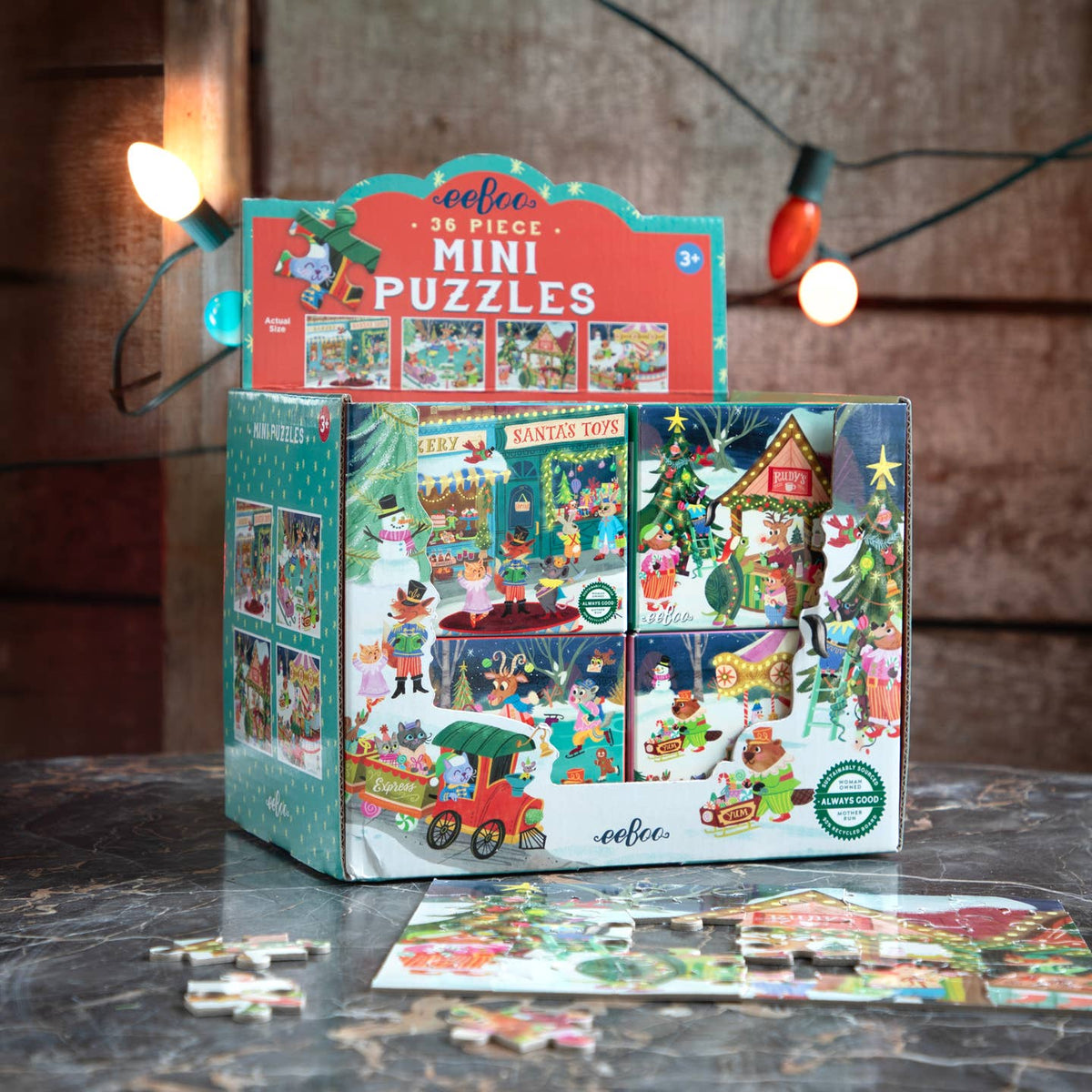 A boxed set of festive mini puzzles displayed on a tabletop, with several loose puzzle pieces in front. The packaging shows colorful holiday scenes and the text 'coffee 36 PIECE MINI PUZZLES.