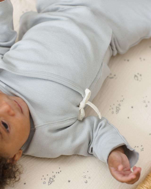 Baby lying on a textured surface wearing a light gray outfit