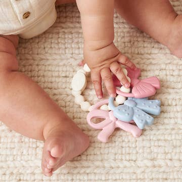 Baby hands playing with colorful teething toys on a textured surface