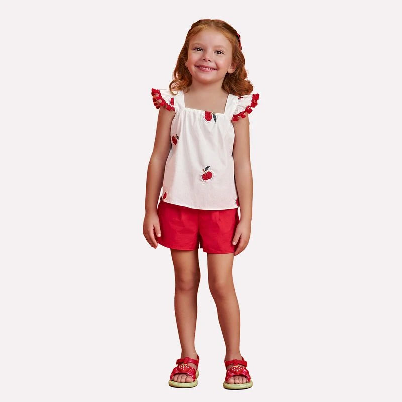 Young girl wearing a white top with red accents and red shorts on a white background
