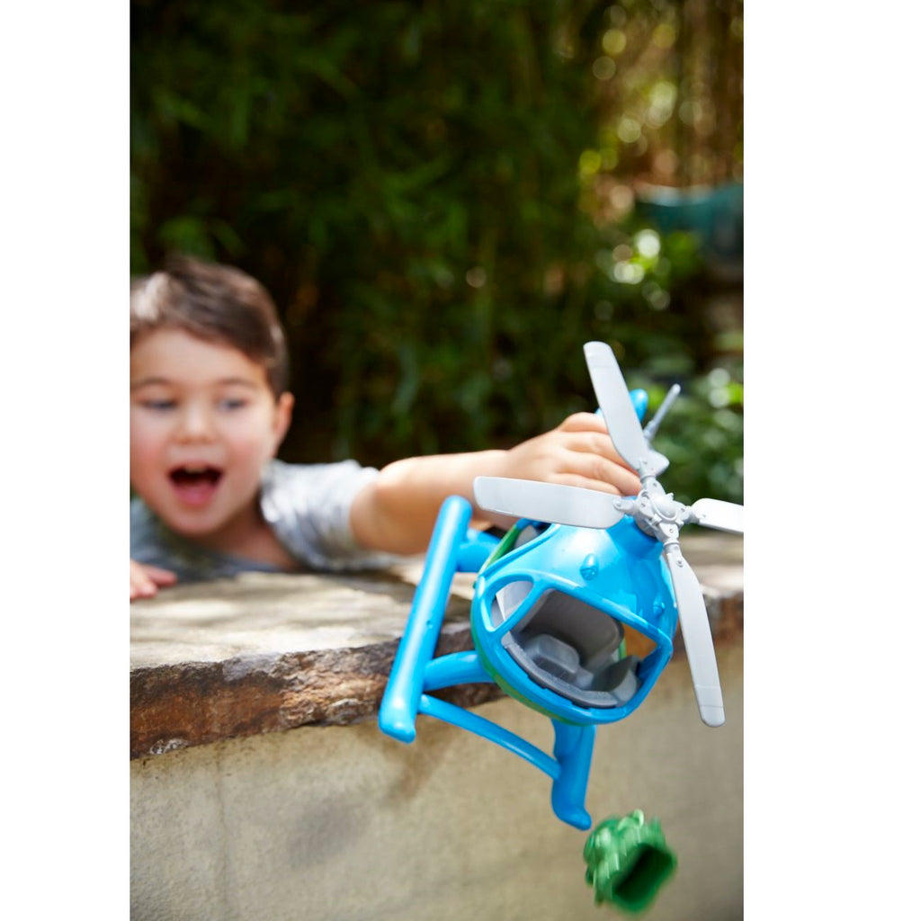Child holding a blue toy helicopter outdoors with greenery in the background