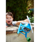 Child holding a blue toy helicopter outdoors with greenery in the background