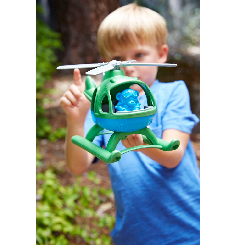 Child holding a green toy helicopter with a blue ball inside, outdoors.