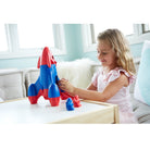 Child playing with a toy rocket on a table in a bright room.