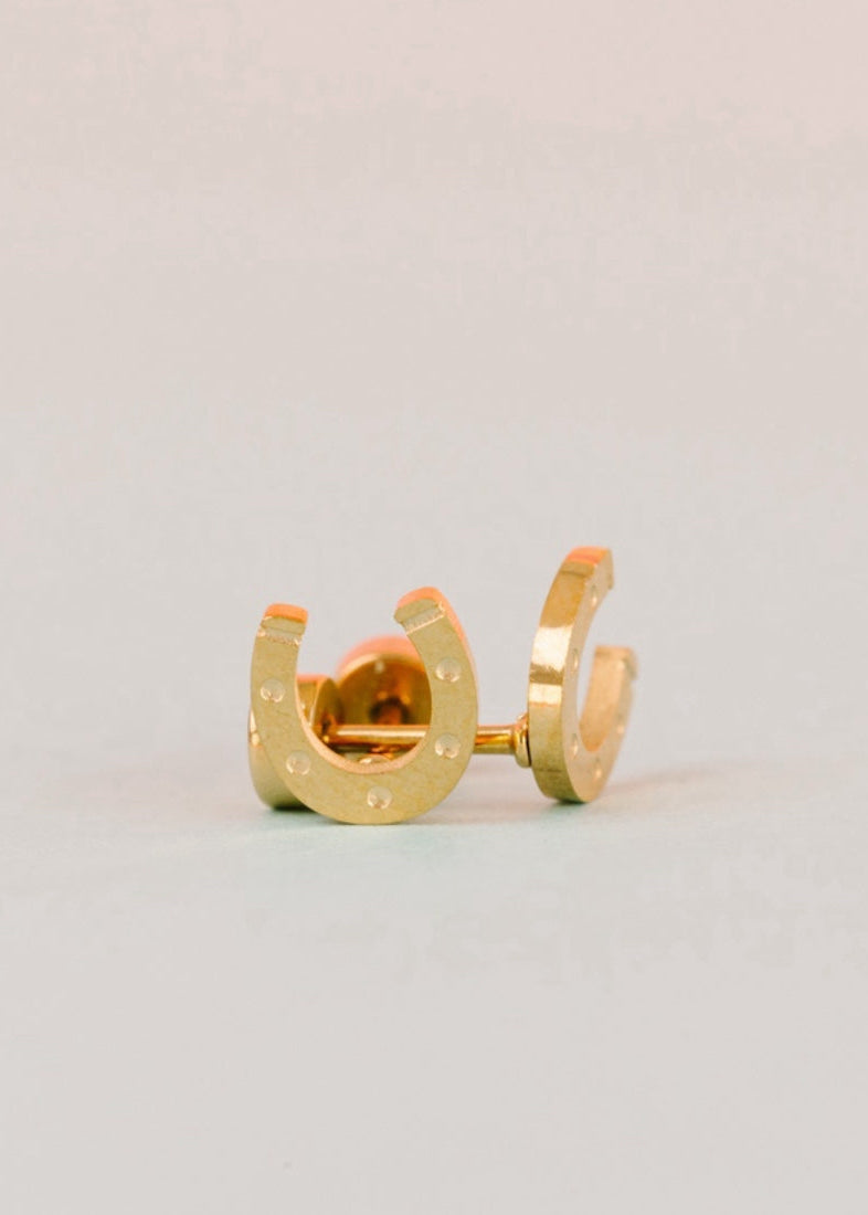 A pair of gold horseshoe stud earrings with small silver rivet details, displayed on a light gray background.