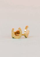 A pair of gold horseshoe stud earrings with small silver rivet details, displayed on a light gray background.