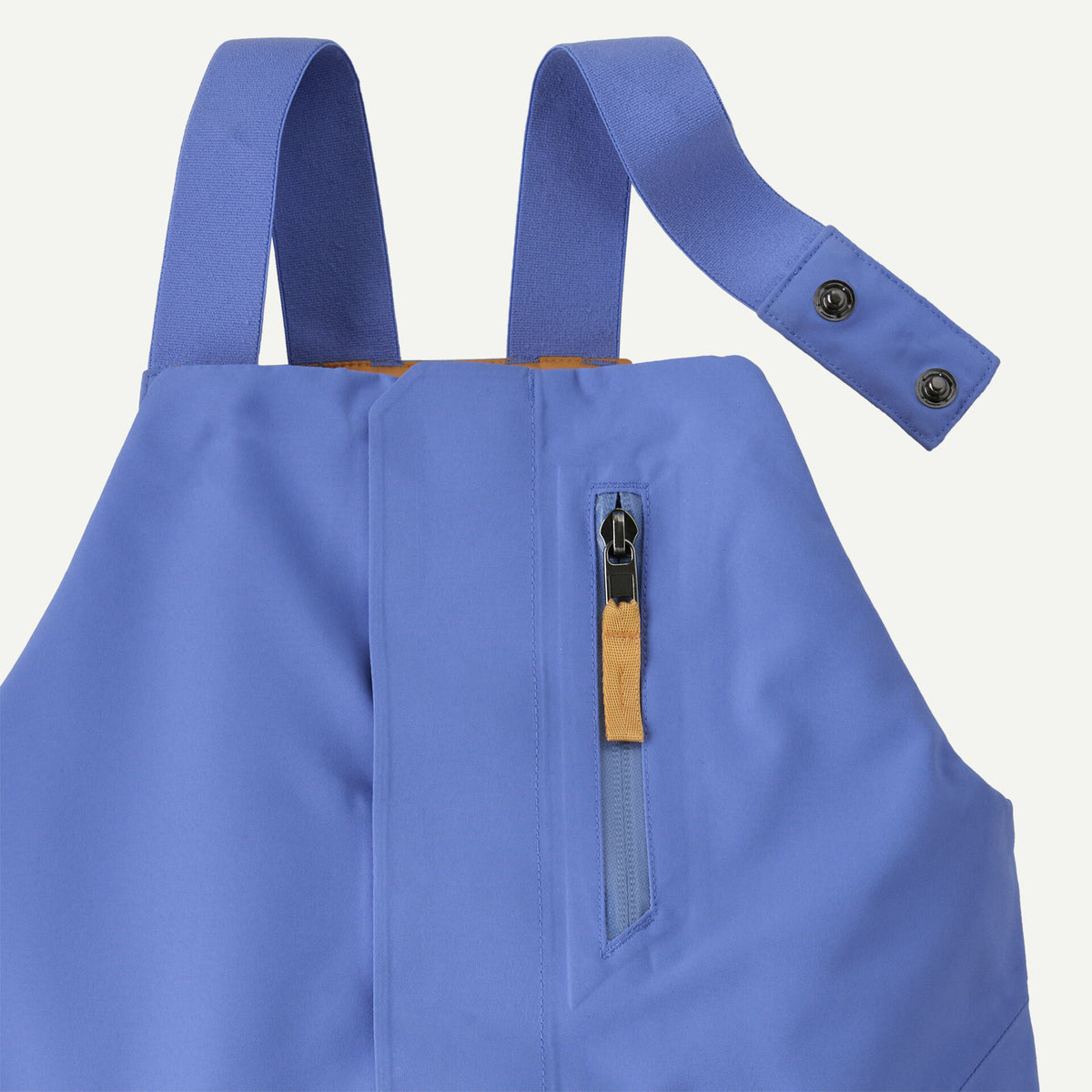 Close-up of a blue waterproof bib jacket showing the shoulder straps with snap buttons and a vertical zippered pocket with a tan pull tab.