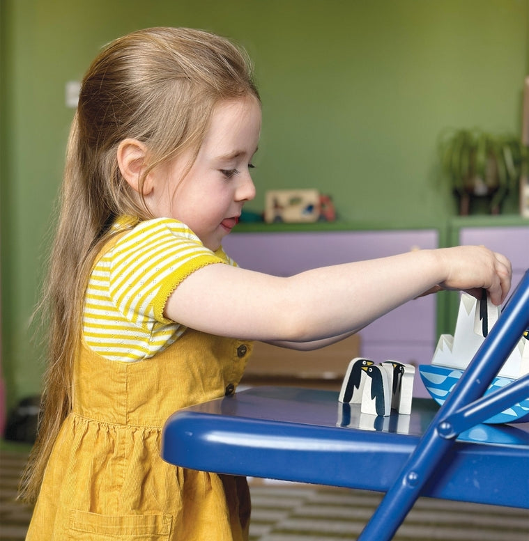 A young child with blonde hair wearing a yellow striped top is focused on playing with a toy at a table.
