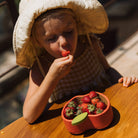Child eating strawberries from a heart-shaped container on a wooden table