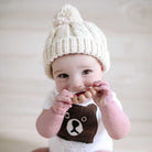 Baby wearing a white knit hat and a onesie with a bear design, holding a toy.