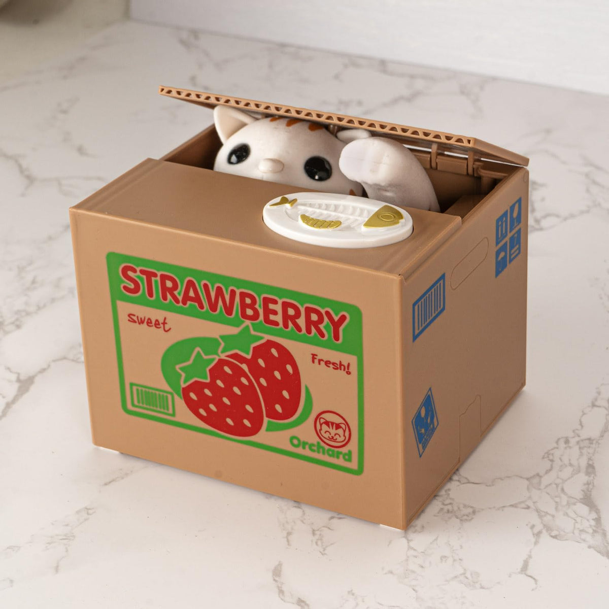 Stuffed animal peeking out from a cardboard box labeled 'Strawberry Orchard' on a marble surface.