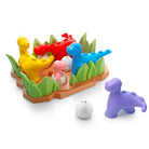 A colorful children's toy set featuring a base with green grass and dinosaur figures in red, yellow, and blue, plus two loose dinosaur figures in purple and pink-and-white egg shapes, photographed on a white background.