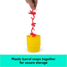 A person holding a vertical chain of red plastic monkeys suspended above a yellow plastic storage barrel for the Barrel of Monkeys Game by Continuum Games, accompanied by text reading "Plastic barrel snaps together for secure storage."