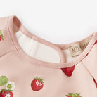 Close-up of a pink garment with strawberry pattern and visible brand label on a white background