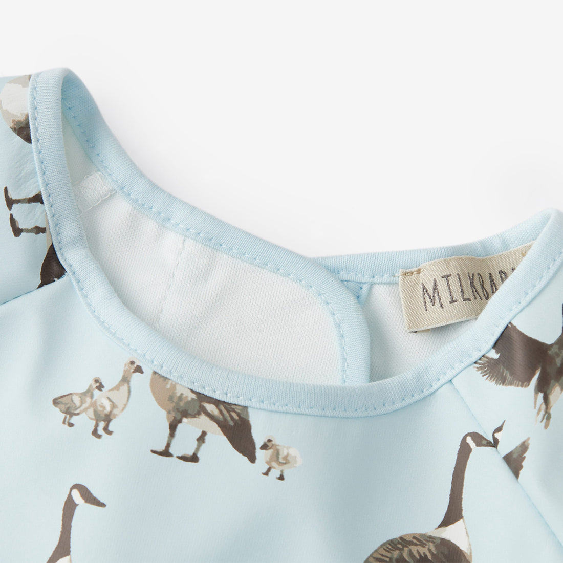 Close-up of a baby outfit with duck pattern and visible brand label on light blue fabric.