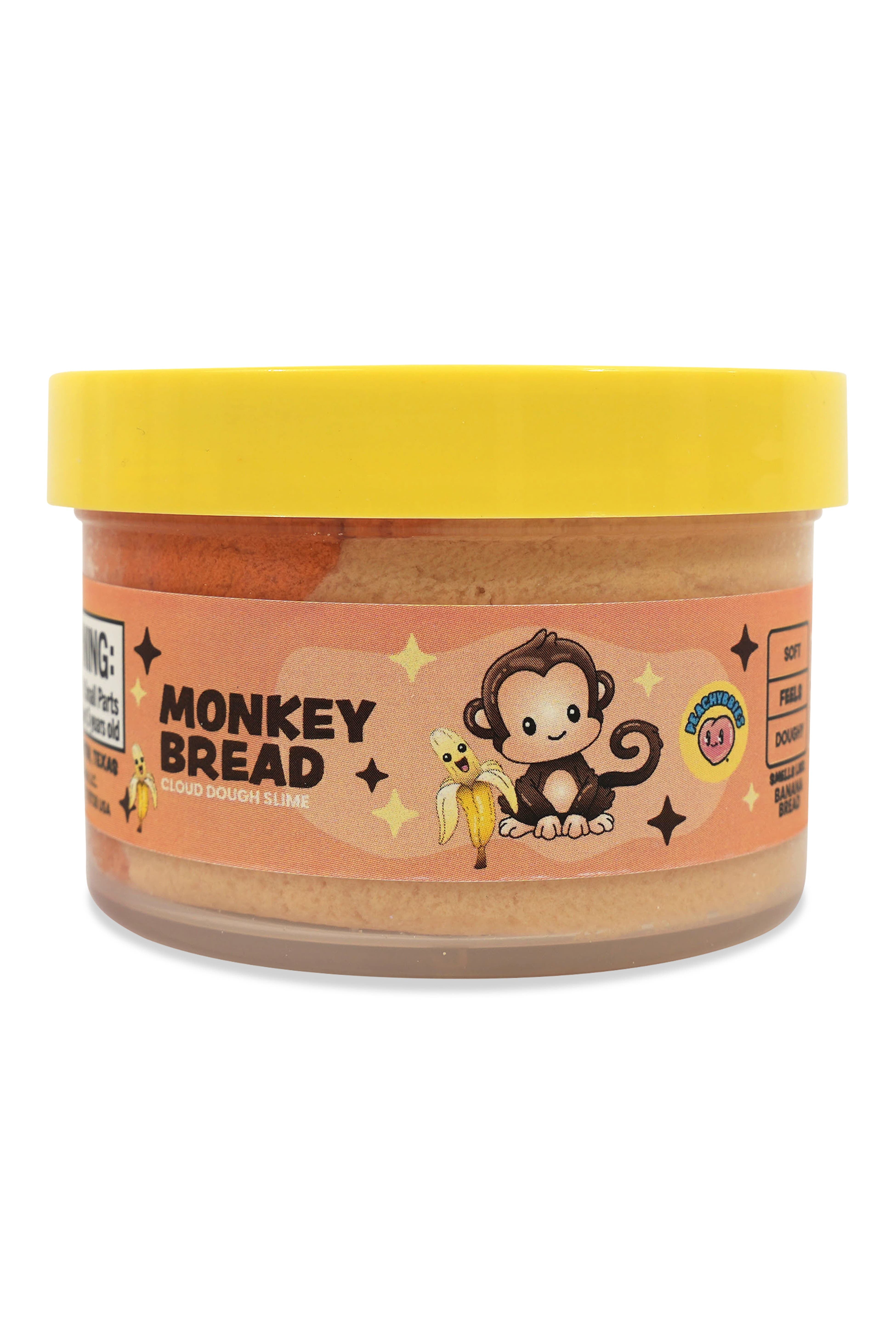 A jar of Monkey Bread Peanut Butter Cookies by Monkey Wrench Cookies, featuring a bright yellow lid and a peach-colored label with a cartoon monkey holding a banana.