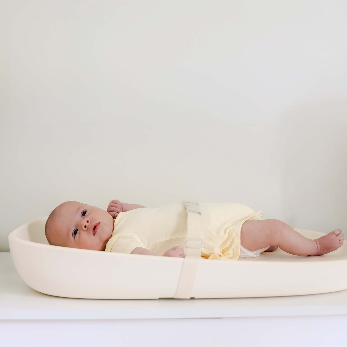 Baby lying on a white bassinet with a plain background