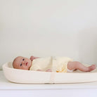 Baby lying on a white bassinet with a plain background
