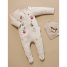 A baby footed sleeper in a warm cream color, decorated with small owl illustrations and tiny orange leaf prints, shown next to a matching cream bib on a solid beige background.