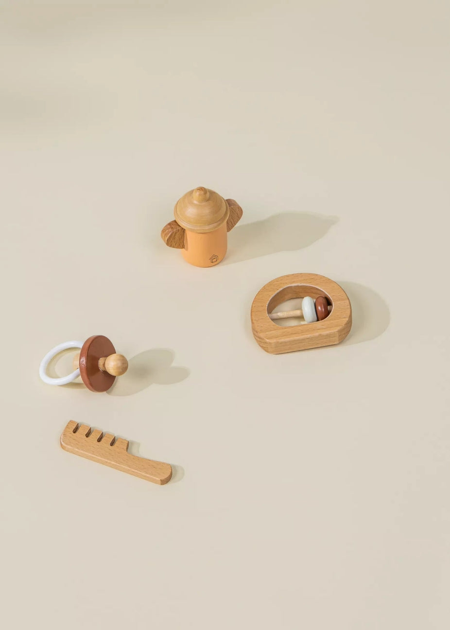 A set of wooden baby toys arranged on a warm beige background, including a small bottle-shaped rattle, a pacifier, a comb, and a circular toy with beads.