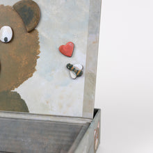 Cartoon bear head with googly eyes and a red heart on a textured wall.