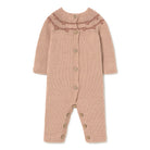 A knitted baby romper in a dusty rose pink color, featuring a ruffled yoke with a darker pink patterned stripe and brown wooden buttons down the front and on the legs, shown against a plain white background.