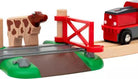 Toy train set with wooden track, cow figure, and red gate on a wooden platform.