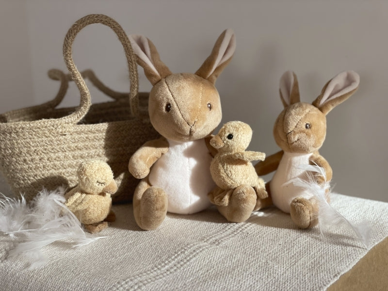 Set of plush bunnies and a basket on a textured surface with a neutral background