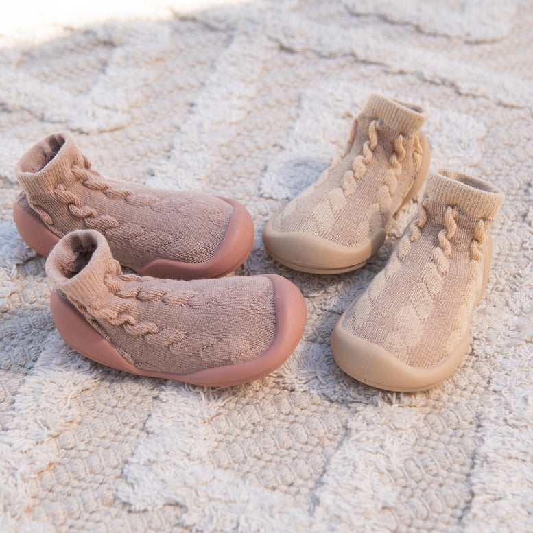 Pair of beige baby shoes with knitted design on a textured surface