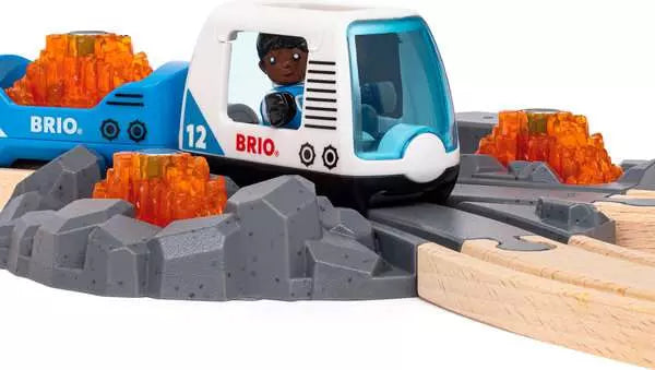 Brio World space train with a blue and white engine and cargo wagons carrying glowing orange minerals, traveling along gray rocky terrain tracks connected to wooden tracks.