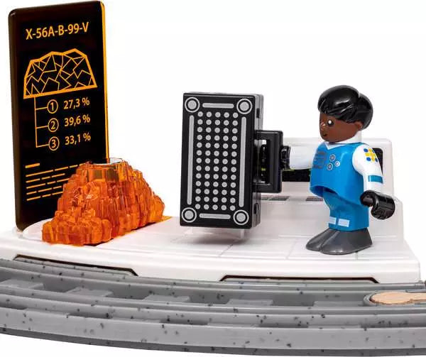 A toy construction vehicle scene with a blue and white minifigure standing beside a black control panel, an orange translucent rock, and a black display screen showing statistics, all on a white and gray vehicle base against a white background.