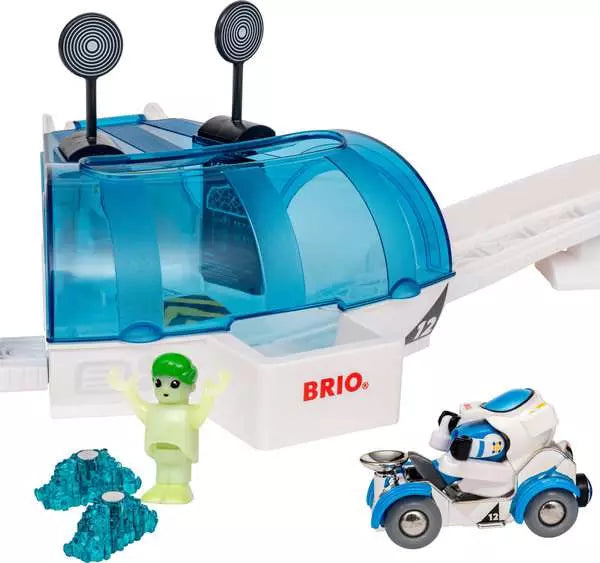 A Brio toy set featuring a white and blue futuristic building or capsule structure with two black antennae, a white slide, a small white and blue vehicle, a light green minifigure, and two blue rock pieces on a plain white background.