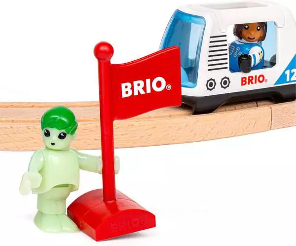 Space Station Set by Brio accessories featuring a glow-in-the-dark alien figure standing next to a red BRIO flag, with a white shuttle wagon and astronaut figure on a wooden track in the background against a white background.