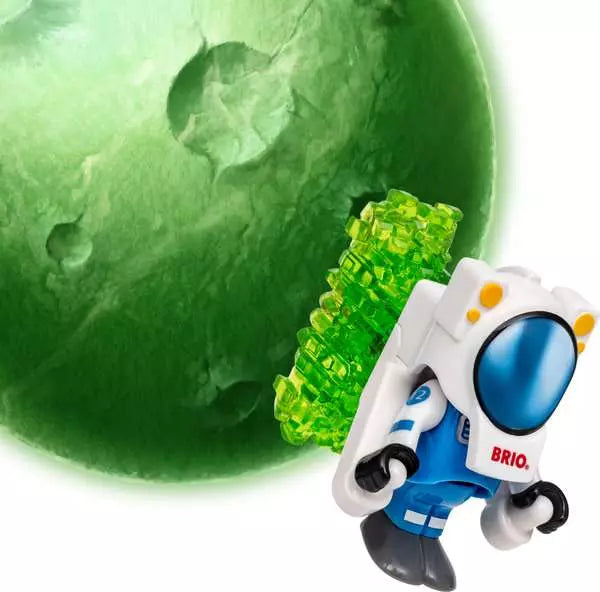 A Space Deluxe Set by Brio astronaut figure wearing a white and blue suit with a glowing green crystal backpack, standing in front of a green planetary background.
