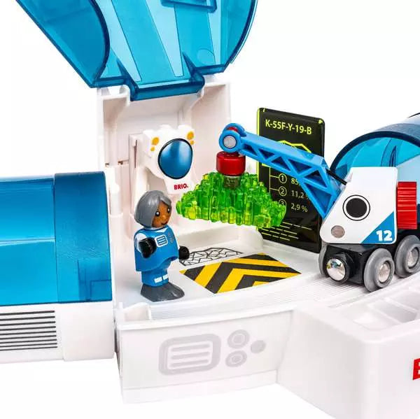 A Space Deluxe Set by Brio astronaut figure standing near an open space station and a cargo crane lifting a green glowing crystal next to a space train.
