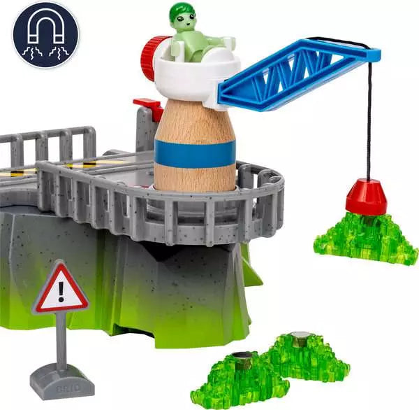 A Space Deluxe Set by Brio grey mountain terrain piece with a blue cargo crane lifting a green glowing crystal, a small warning sign, and a circular magnet icon in the top-left corner.