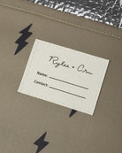 A close-up of a kraft paper envelope or gift bag with black lightning-bolt graphics, featuring a white paper insert card with printed text fields.