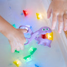 Children playing with a purple ghost toy in water, surrounded by colorful lights.