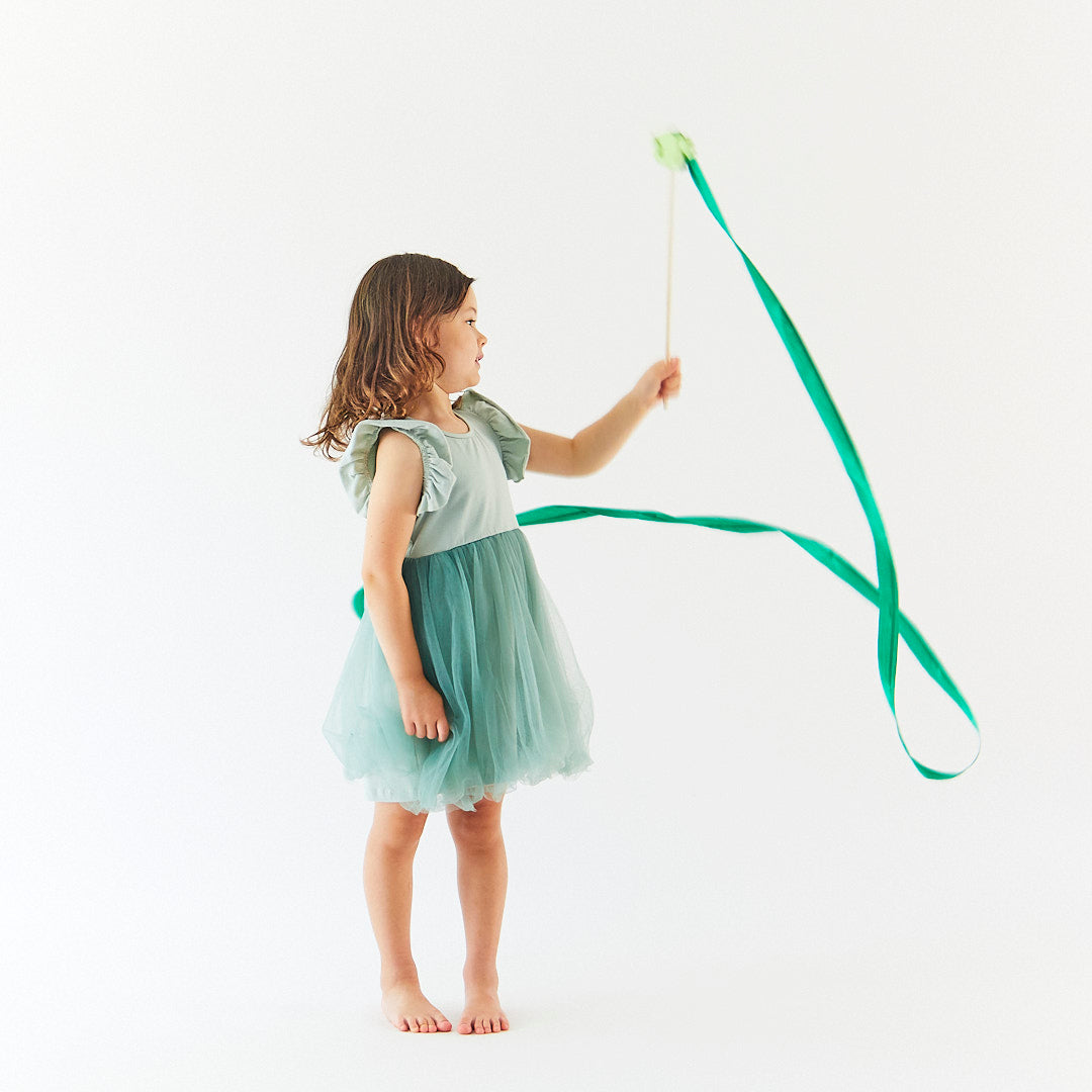 Young girl in a green dress holding a long, thin object against a white background