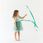 Young girl in a green dress holding a long, thin object against a white background