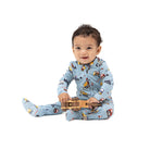 A baby sitting on a white background wearing a light blue one-piece pajama with a construction vehicle print and holding a small wooden toy truck.