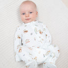 A baby lying on a textured white blanket, wearing a white footed sleep sack with a colorful duck and fish pattern.
