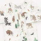 A close-up of a baby zip-up sleeper by Angel Dog, featuring an all-over safari animal print on a white background. The print includes brown bison, gray bears, green pine trees, and small red and orange birds.
