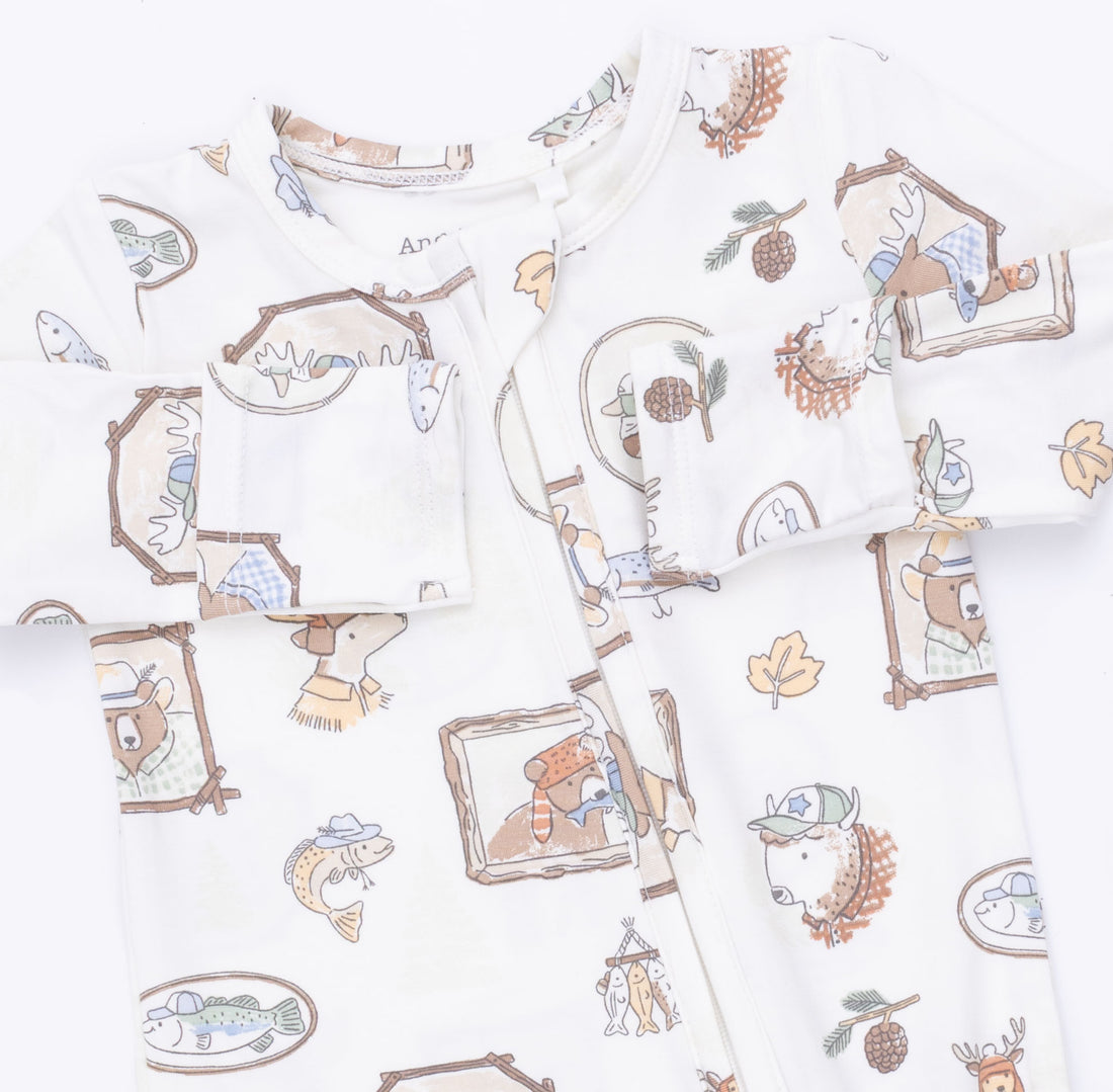 A baby long-sleeve romper in white, featuring a whimsical cartoon animal and nature print including bears, fish, pinecones, and leaves in soft brown, beige, and muted blue tones.