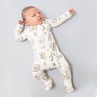 A sleeping newborn baby wearing a long-sleeve footed sleeper with a whimsical animal and house pattern, lying on a light gray background.