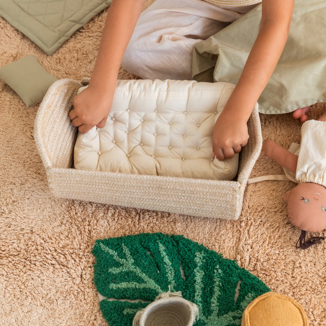 Child playing with a doll and a woven basket on a carpeted floor.