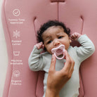 Baby lying on a pink cushion with a pacifier, surrounded by text icons indicating features.