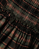 Close-up of a smocked plaid fabric with horizontal gathered seams, featuring a pattern of black, olive green, and rust red.