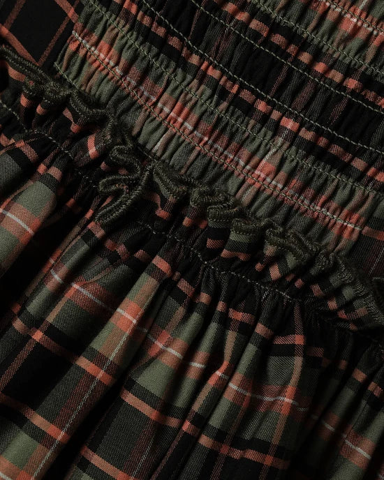 Close-up of a smocked plaid fabric with horizontal gathered seams, featuring a pattern of black, olive green, and rust red.